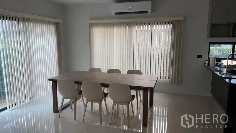 Detached House for rent in Bang Kapi, Bangkok - Dining area with six white chairs around a wooden table beside large windows.