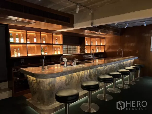 零售空间 出租在Watthana, Bangkok - 大理石台面的吧台，背光酒架与一排高脚凳。