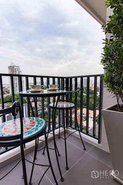 公寓 出售在Watthana, Bangkok - 转角阳台配高脚圆桌椅，眺望都市天际线。