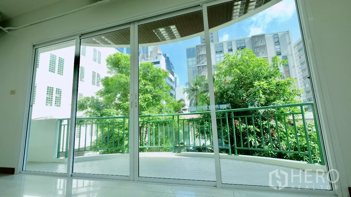 Office Space for rent - View through floor-to-ceiling sliding doors to a curved balcony with green railings and city buildings beyond.