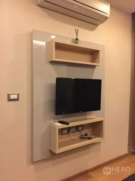 Condominium for rent in Ratchathewi, Bangkok - Wall-mounted flat-screen TV with floating shelves and an air conditioner above.