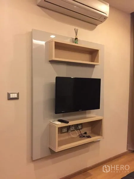 Condominium for rent in Ratchathewi, Bangkok - Wall-mounted flat-screen TV with floating shelves and an air conditioner above.
