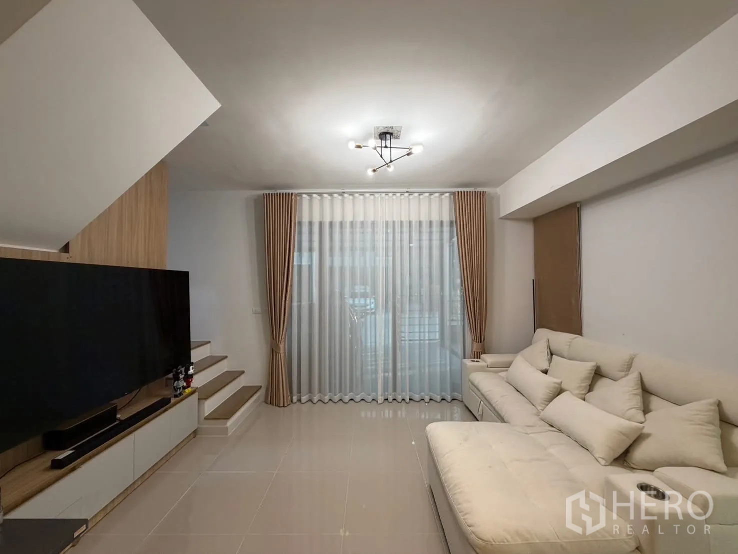 Townhouse for rent in Bang Phli, Samut Prakan - Living room facing staircase and media wall with a large TV and sheer curtains.