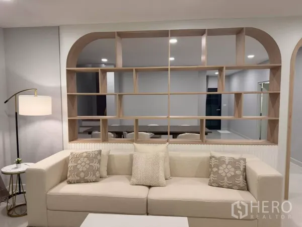 独立式住宅 出租在Bang Phli, Samut Prakan - 客厅一角，米色沙发、开放式隔断书架与落地灯，配色素雅。