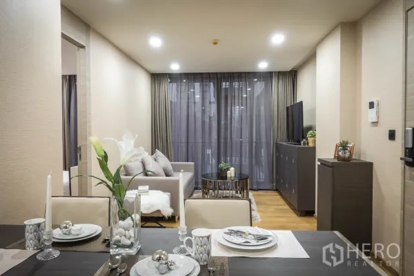 公寓 出租在Pathum Wan, Bangkok - 开放式客餐厅，灰色沙发、电视柜与落地窗帘，通向阳台。