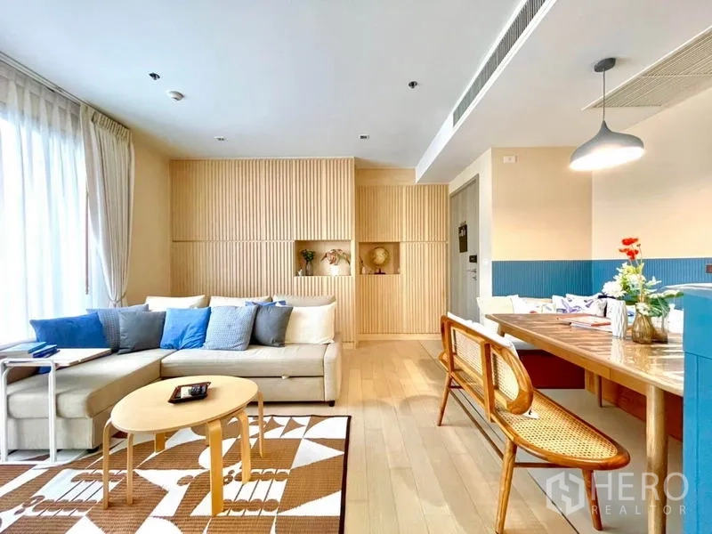 คอนโด ให้เช่าหรือขายในWatthana, Bangkok - ห้องนั่งเล่นโปร่งสบาย โซฟาตัวแอล หมอนสีน้ำเงิน ผนังไม้เซาะร่อง และชุดทานข้าว