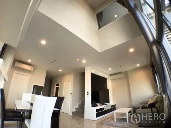 Condominium for rent in Khlong Toei, Bangkok - Double-height living space with staircase and expansive windows for natural light.