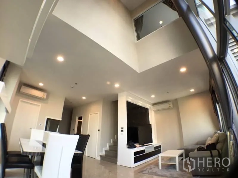 Condominium for rent in Khlong Toei, Bangkok - Double-height living space with staircase and expansive windows for natural light.