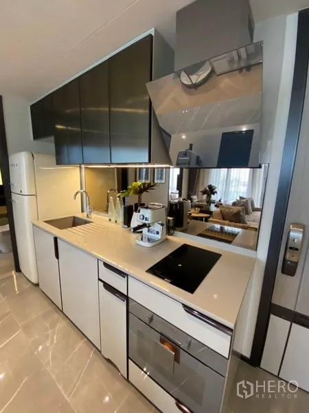 Condominium for rent in Watthana, Bangkok - Sleek kitchenette with induction hob, built-in oven, mirrored backsplash and tall cabinets.