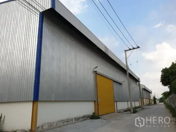 Warehouse for rent in Lat Krabang, Bangkok - Street-side view of metal-clad warehouse with yellow roller doors and utility poles.