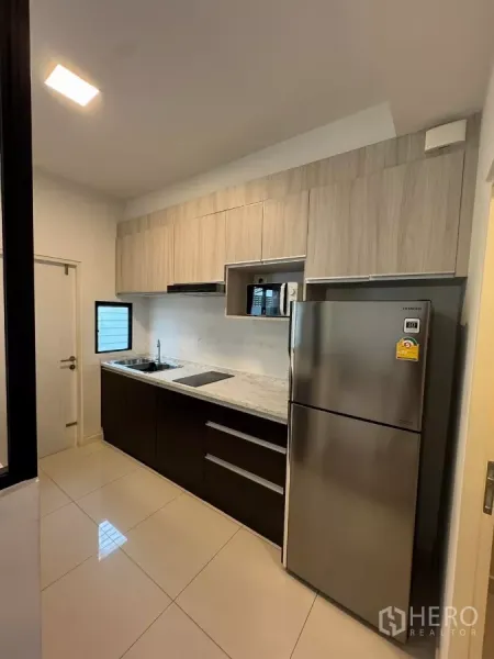 Townhouse for rent in Bang Phli, Samut Prakan - Fitted kitchen with wood cabinets, marble-look counter, hob, sink, microwave niche, and stainless fridge.