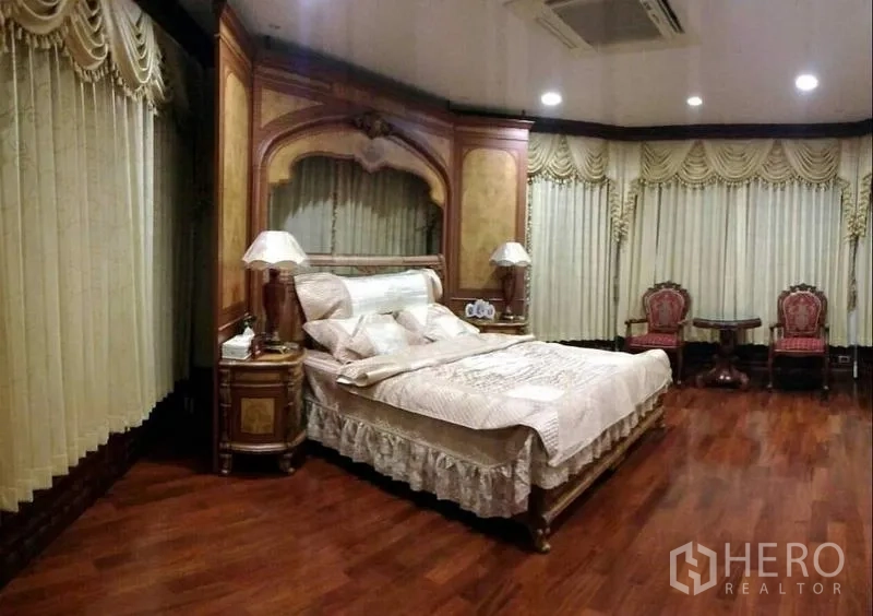 Detached House for sale in Phra Samut Chedi, Samut Prakan - Large master bedroom with wood floors, carved headboard, layered drapes and recessed lighting.