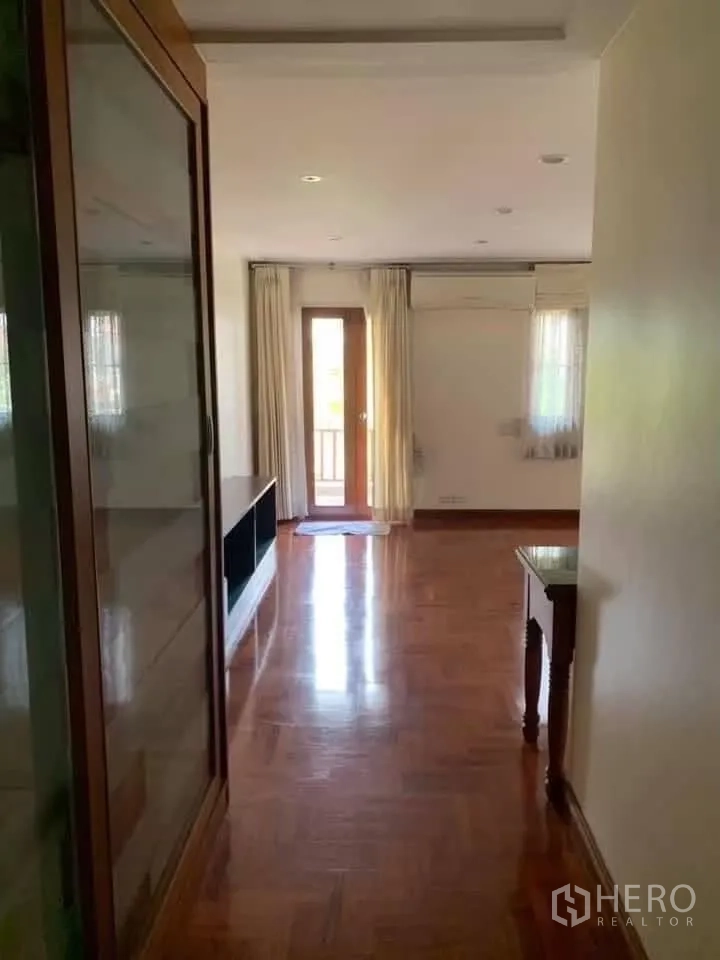 Townhouse for rent in Watthana, Bangkok - Hallway with polished wooden floors leading to a balcony door and windows with curtains.