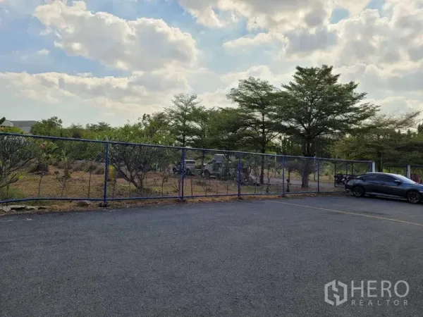 货栈 出租在Phra Khanong, Bangkok - 曼谷帕卡农仓库的室外柏油停车区，链式围栏与成排树木。