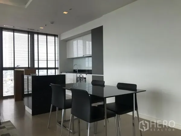 Condominium for rent or sale in Khlong San, Bangkok - Dining area beside a modern kitchen with glossy black table and wall-to-wall windows.