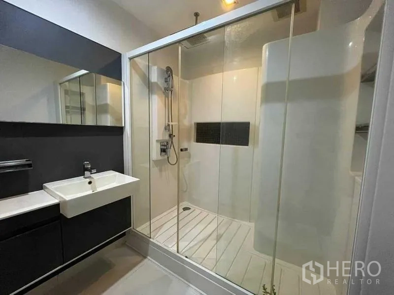 Condominium for sale - Modern bathroom featuring a large glass-enclosed shower and wall-mounted sink with mirror.