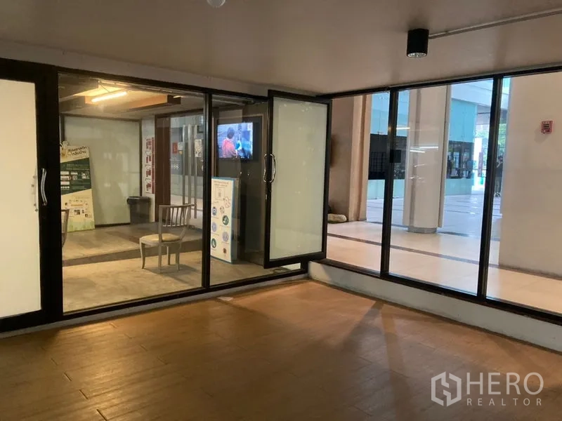 零售空间 出租在Khlong Toei, Bangkok - 店内朝向玻璃入口，可通往有顶广场，木纹地面清晰可见。