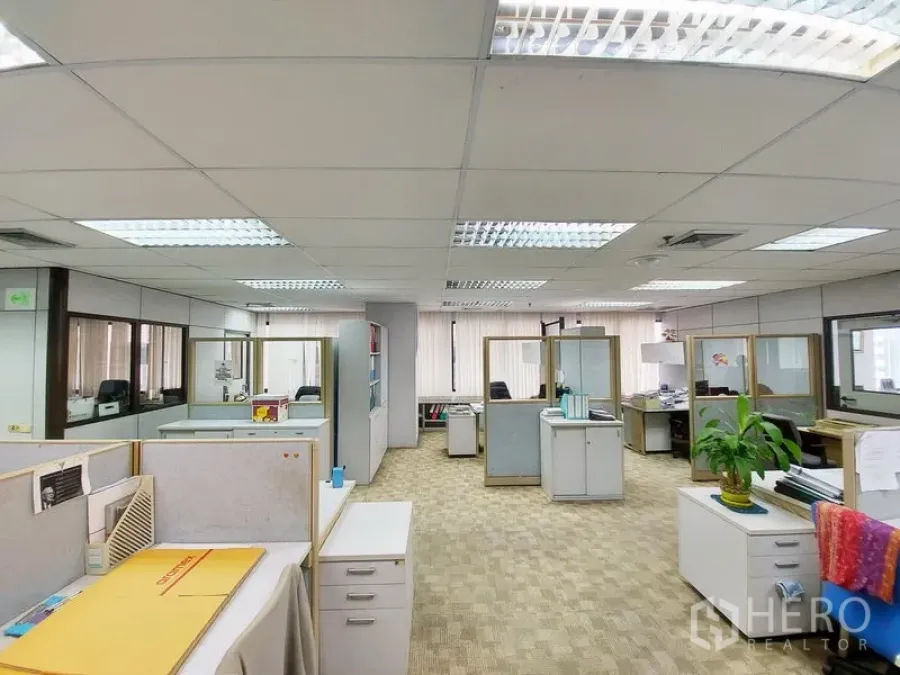 สำนักงาน ให้เช่าในRatchathewi, Bangkok - พื้นที่ออฟฟิศแบบเปิด มีโต๊ะทำงานกั้นบูธ พื้นพรม แสงไฟฟลูออเรสเซนต์ และหน้าต่างบานใหญ่รับแสงธรรมชาติ