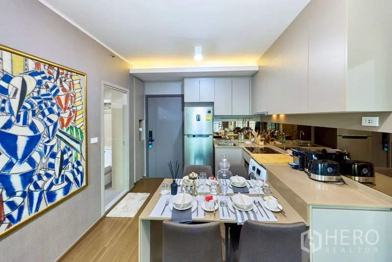Condominium for rent in Phra Khanong, Bangkok - Table set for four beside a compact kitchen with appliances and a washer in a Sukhumvit condo.