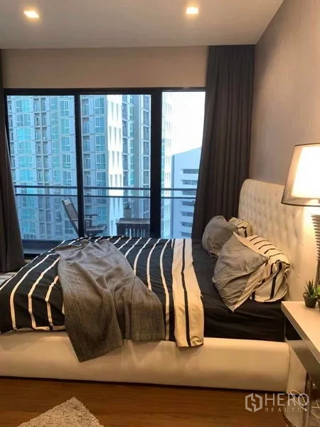 Condominium for rent or sale in Huai Khwang, Bangkok - Master bedroom with upholstered headboard and balcony access overlooking the city.