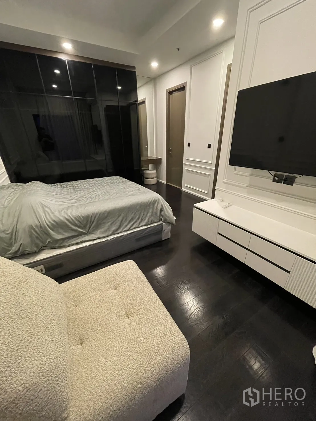 Condominium for rent in Watthana, Bangkok - Primary bedroom with dark wood floor, wall-mounted TV, and glossy wardrobe.