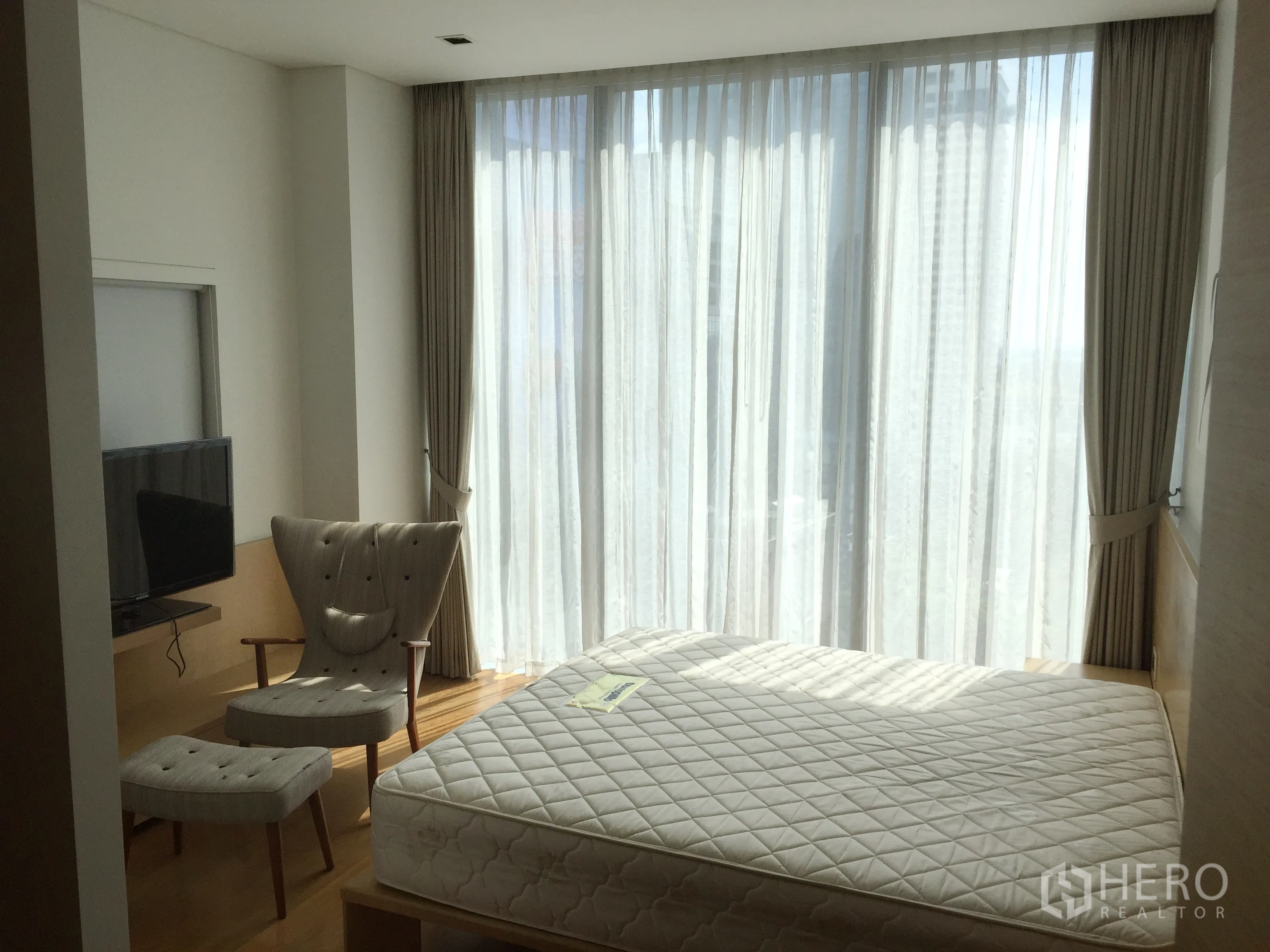 公寓 出租在Bang Rak, Bangkok - 明亮卧室，超大落地窗，休闲椅与电视，浅色木地板。