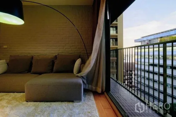 公寓 出租在Watthana, Bangkok - 客厅阳台，城市景观、深色栏杆，窗帘飘动在沙发旁。