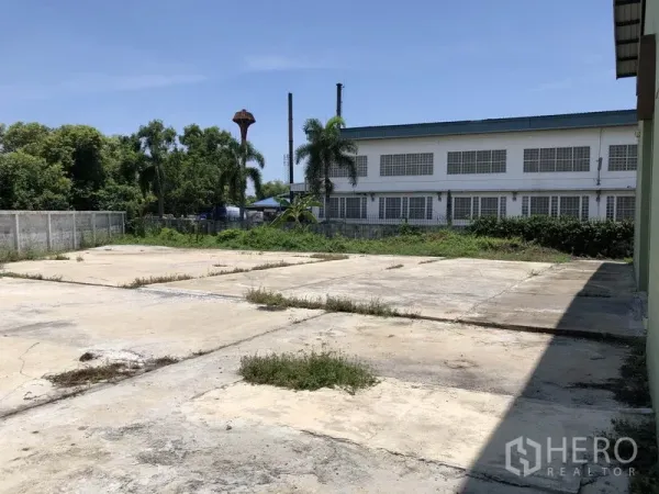 工厂 出租在Pathum Thani - 厂房外的铺装院场与围墙，周边有树木