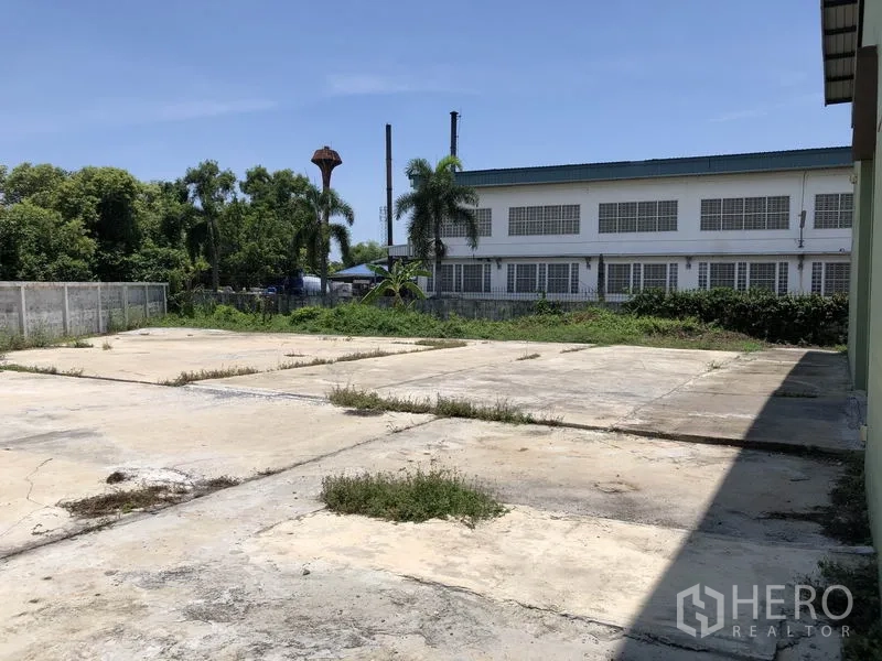 工厂 出租在Pathum Thani - 厂房外的铺装院场与围墙，周边有树木