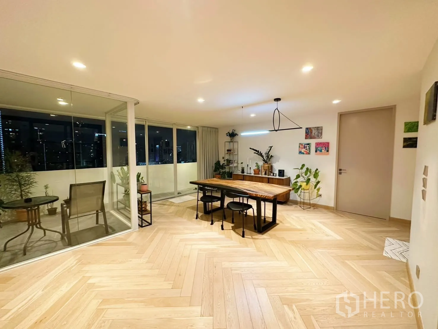 Condominium for rent or sale in Watthana, Bangkok - Dining zone opening to a spacious balcony with plants at night.