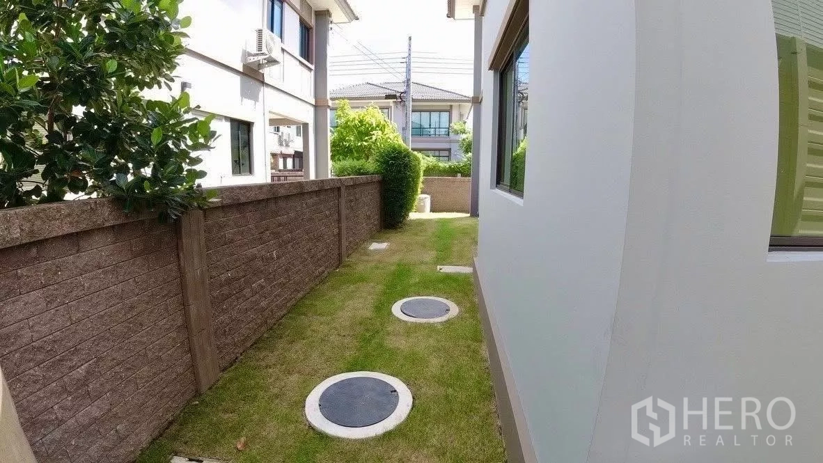 独立式住宅 出租或出售在Bang Phli, Samut Prakan - 房屋侧院草地小径，沿墙设检修井盖。