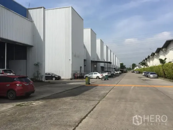 工厂 出租在Khlong Luang, Pathum Thani - 园区内成排仓库建筑，宽阔混凝土车道与道路两侧停车位。