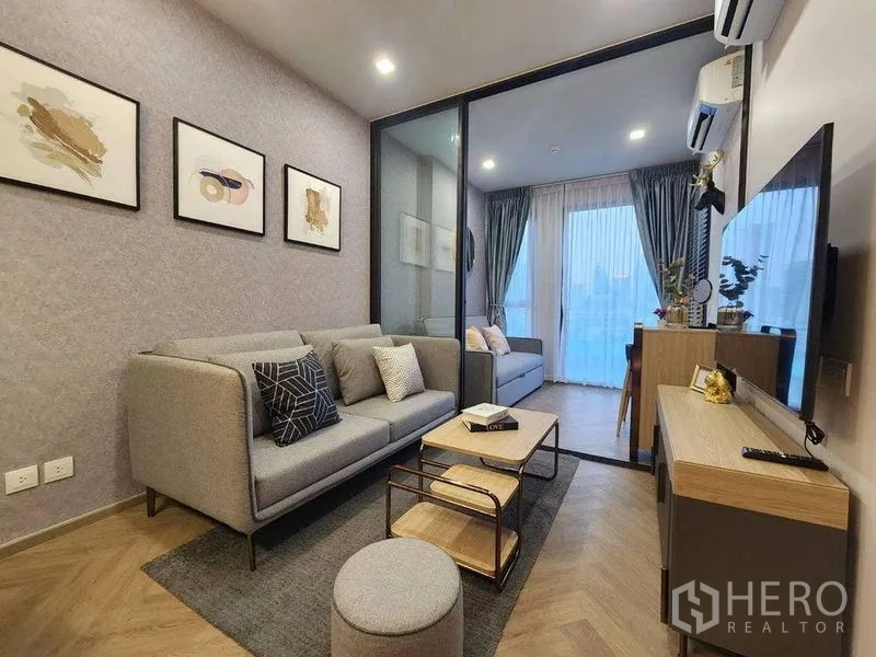Condominium for rent in Bang Rak, Bangkok - Living room with gray sofa, TV console and glass partition to a multipurpose room.
