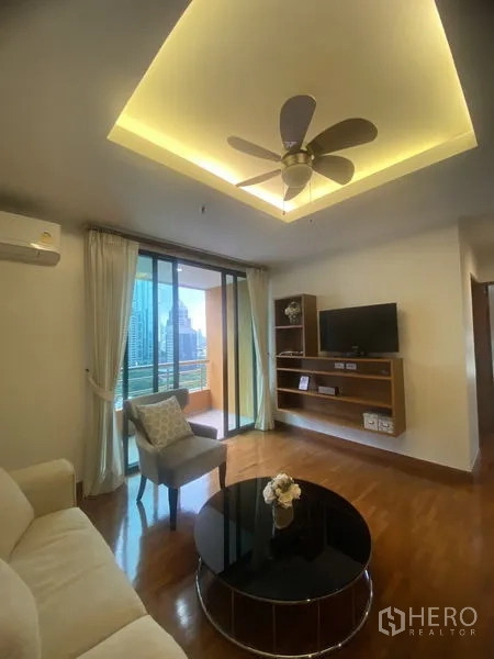 คอนโด ให้เช่าในPathum Wan, Bangkok - ห้องนั่งเล่นอบอุ่น พัดลมเพดาน ผนังบิวท์อินติดทีวี และประตูกระจกสู่ระเบียงมองเห็นวิวเมือง