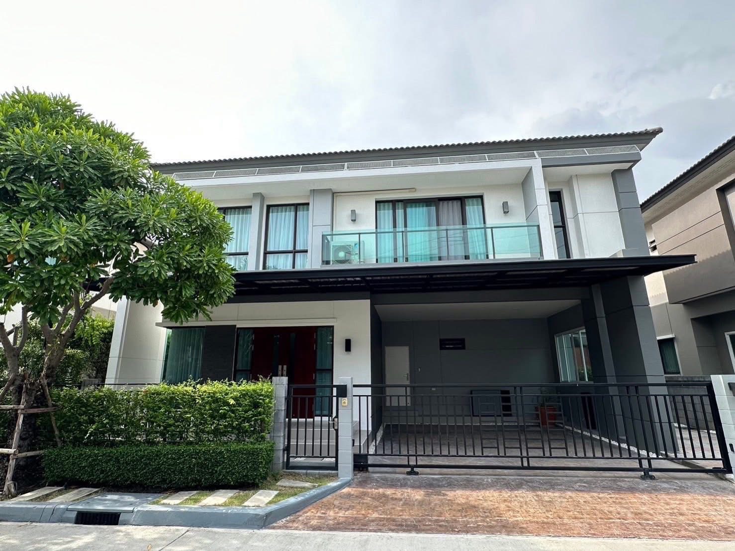 Detached House for rent in Bang Phli, Samut Prakan - Contemporary two-storey detached house exterior with glass balcony, gated covered carport and trimmed hedge.