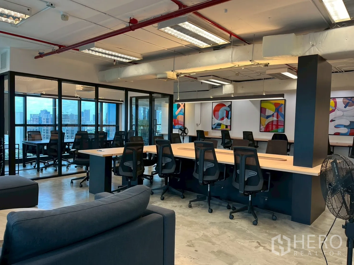 办公室 for rent in Watthana, Bangkok - 多组办公桌椅、沙发与玻璃墙，墙面装饰画鲜艳。