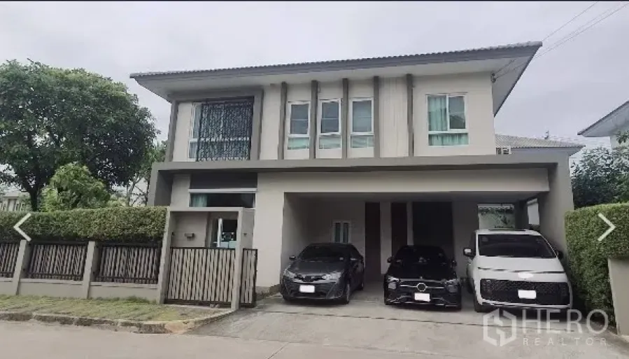 Detached House for rent in Don Mueang, Bangkok - Front view of the two-storey house with hedge-lined fence and a wide driveway.