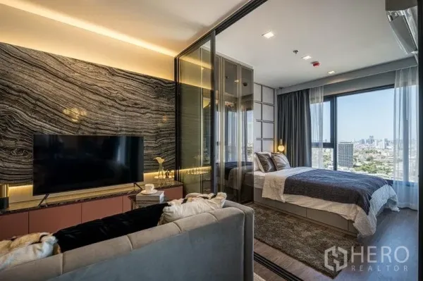 Condominium for sale in Chatuchak, Bangkok - Modern living room with stone-pattern feature wall, TV console, and glass-partitioned bedroom overlooking the Bangkok skyline.