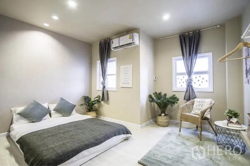 ทาวน์เฮาส์ ให้เช่าในKhlong Toei, Bangkok - ห้องนอนกว้าง เตียงวางต่ำ หน้าต่างสองบาน ผ้าม่านสีเทา แอร์และต้นไม้แต่ง