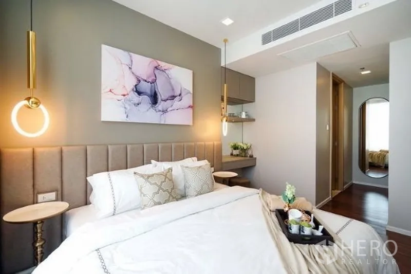 คอนโด ให้เช่าในWatthana, Bangkok - ห้องนอนมาสเตอร์โทนอบอุ่น หัวเตียงบุผ้า ไฟห้อยสีทอง ภาพตกแต่ง มุมโต๊ะทำงาน และพื้นไม้