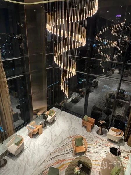 公寓 出租在Ratchathewi, Bangkok - 夜间大堂中庭，螺旋吊灯与休息座椅。