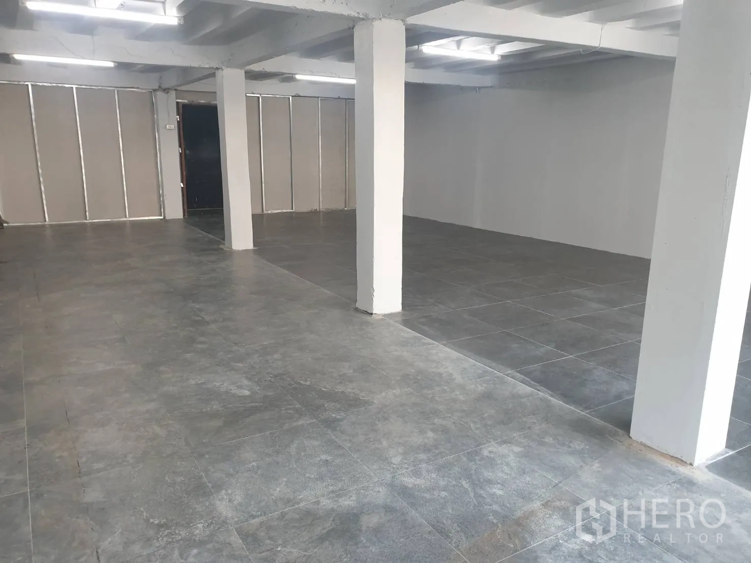 零售空间 出租在Khlong Toei, Bangkok - 开放式零售室内，灰色瓷砖地面、白色承重柱与明亮长条灯。