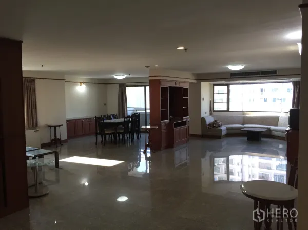 คอนโด ให้เช่าในWatthana, Bangkok - พื้นที่นั่งเล่นและรับประทานอาหารแบบโอเพนแปลนในคอนโดเขตวัฒนา กรุงเทพฯ พื้นหินขัด เฟอร์นิเจอร์บิวท์อิน หน้าต่างกระจกบานโค้งและโซฟารูปตัวแอล