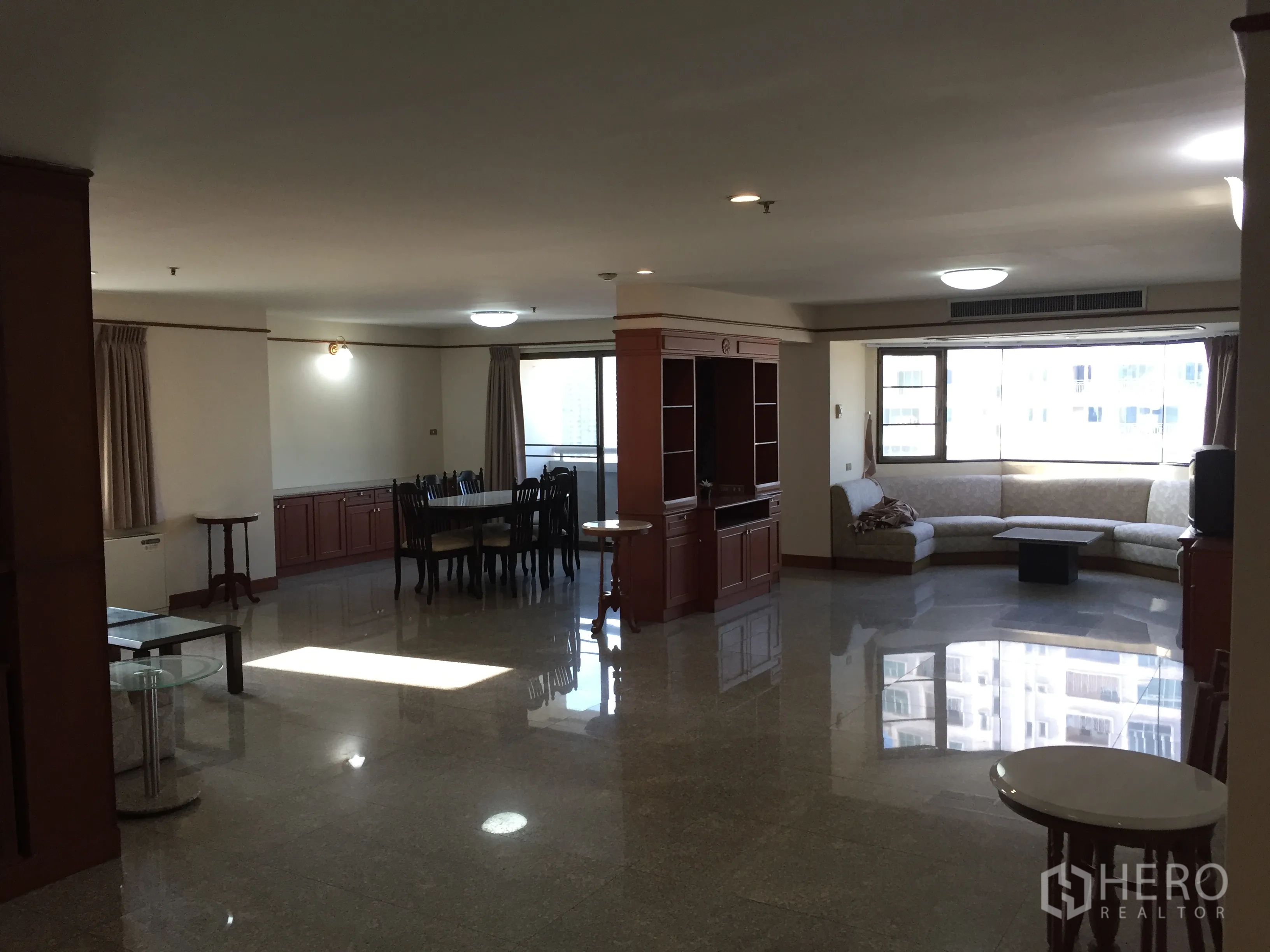 คอนโด ให้เช่าในWatthana, Bangkok - พื้นที่นั่งเล่นและรับประทานอาหารแบบโอเพนแปลนในคอนโดเขตวัฒนา กรุงเทพฯ พื้นหินขัด เฟอร์นิเจอร์บิวท์อิน หน้าต่างกระจกบานโค้งและโซฟารูปตัวแอล