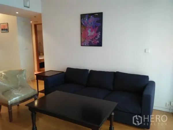 Condominium for rent in Sathon, Bangkok - Cozy seating area with navy sofa, armchair and coffee table against a white wall.