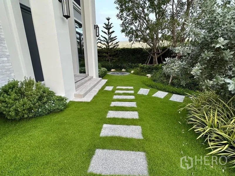 บ้าน ขายในLat Krabang, Bangkok - สวนหน้าบ้านมีทางเดินแผ่นหิน พุ่มไม้ตัดแต่ง และต้นไม้