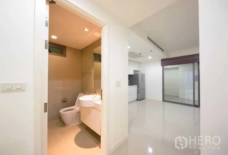 Condominium for sale - Clean bathroom next to an open-plan area with glossy floors and a compact white kitchen.