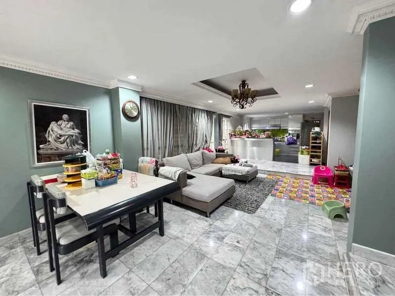 Detached House for rent in Suan Luang, Bangkok - Open-plan living and dining area with marble floors, L-shaped sofa, chandelier and a modern kitchen island.