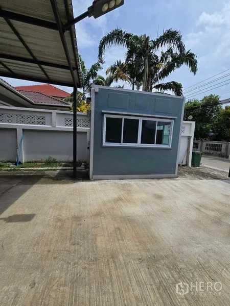 Warehouse for rent in Don Mueang, Bangkok - Detached modular office with window inside the yard, with palm trees nearby.
