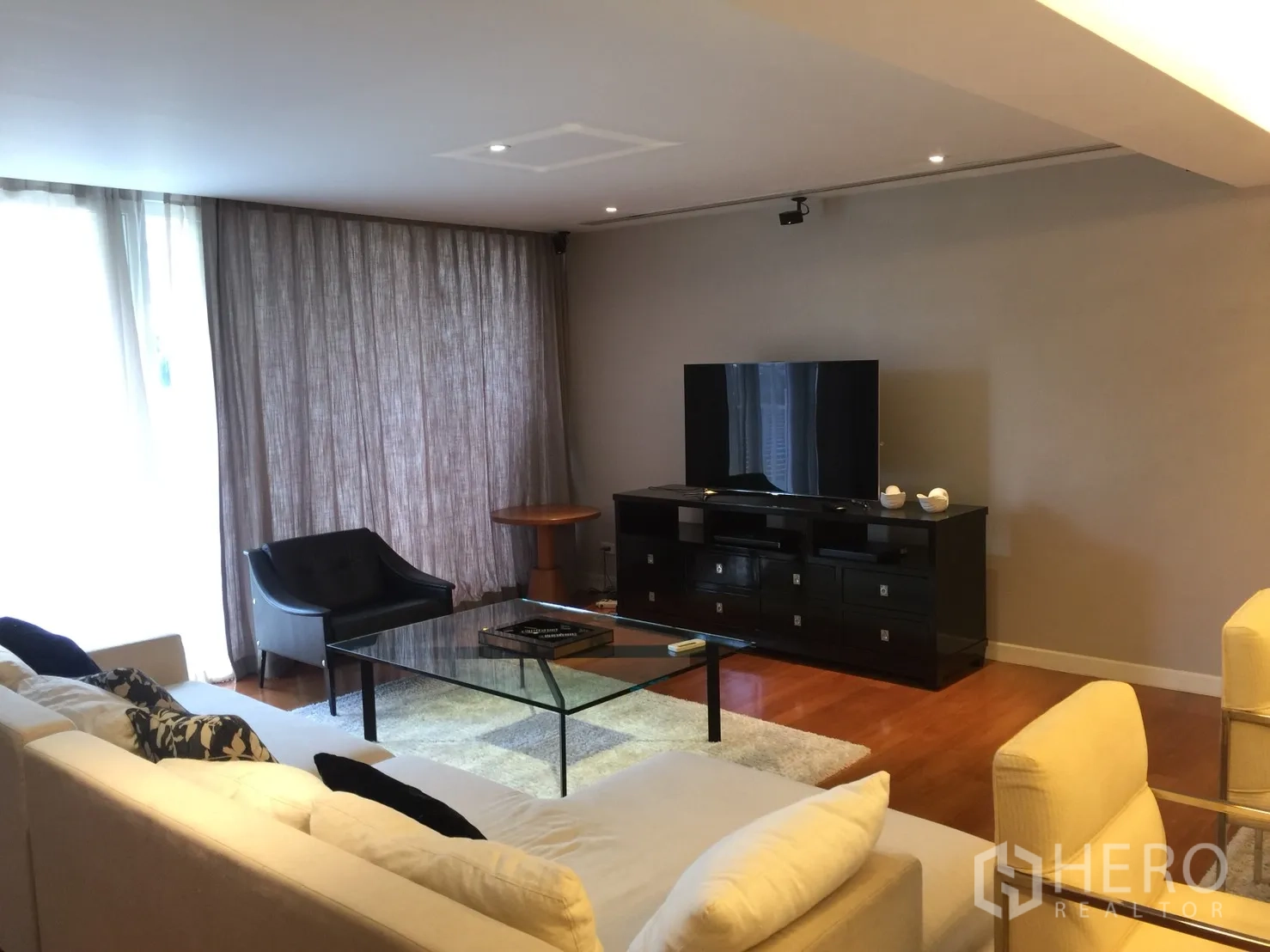 คอนโด ให้เช่าในWatthana, Bangkok - ห้องนั่งเล่นกว้าง โซฟาเข้ามุม โต๊ะกระจก ชั้นวางทีวี และผ้าม่านสูงจรดเพดาน